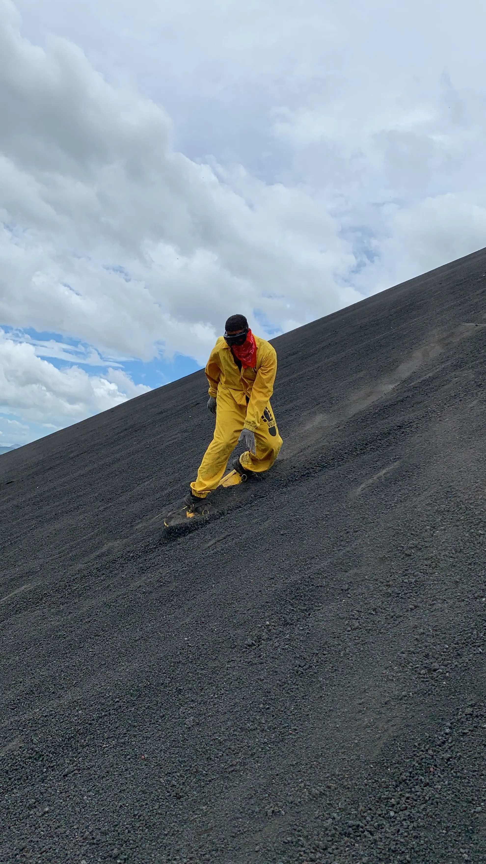 Ahmed Mahrakawy in yellow jumpsuit sliding down a steep volcano under a cloudy sky.