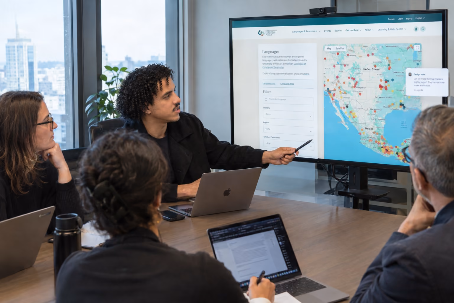Four people in a meeting room with laptops, Ahmed is pointing at a large screen showing a United States and Mexico map with data points and a sidebar filter menu.